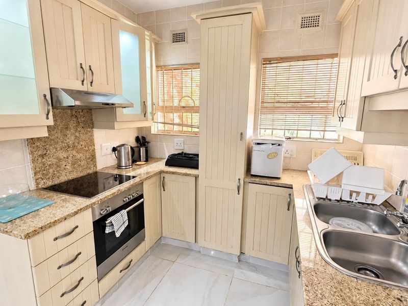 A functional kitchen featuring cream-colored cabinetry, granite countertops, a built-in oven with electric hob, and a double basin sink with tiled finishes.