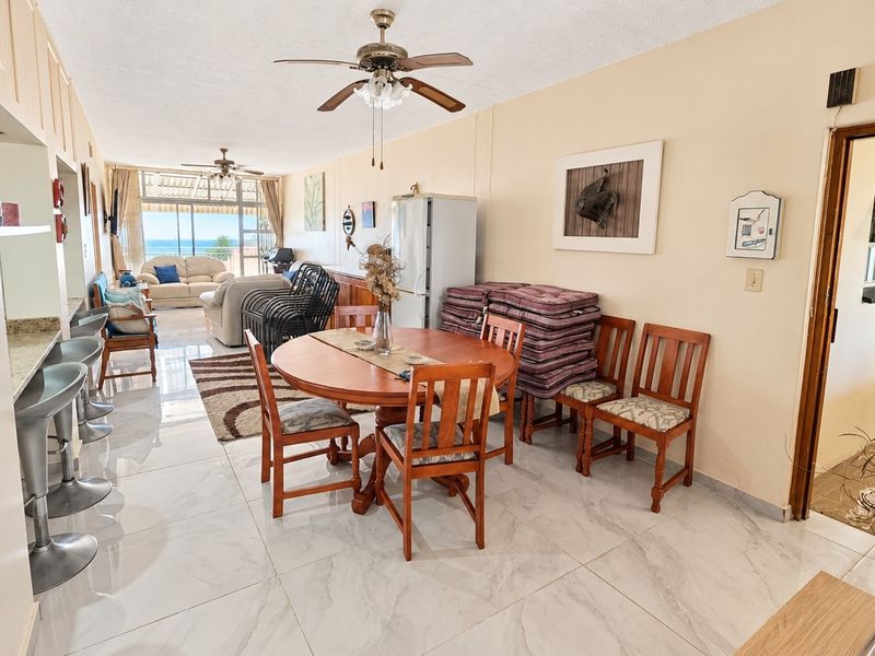 Spacious open-plan living and dining area featuring tiled flooring, ceiling fans, and direct access to a balcony with ocean views.