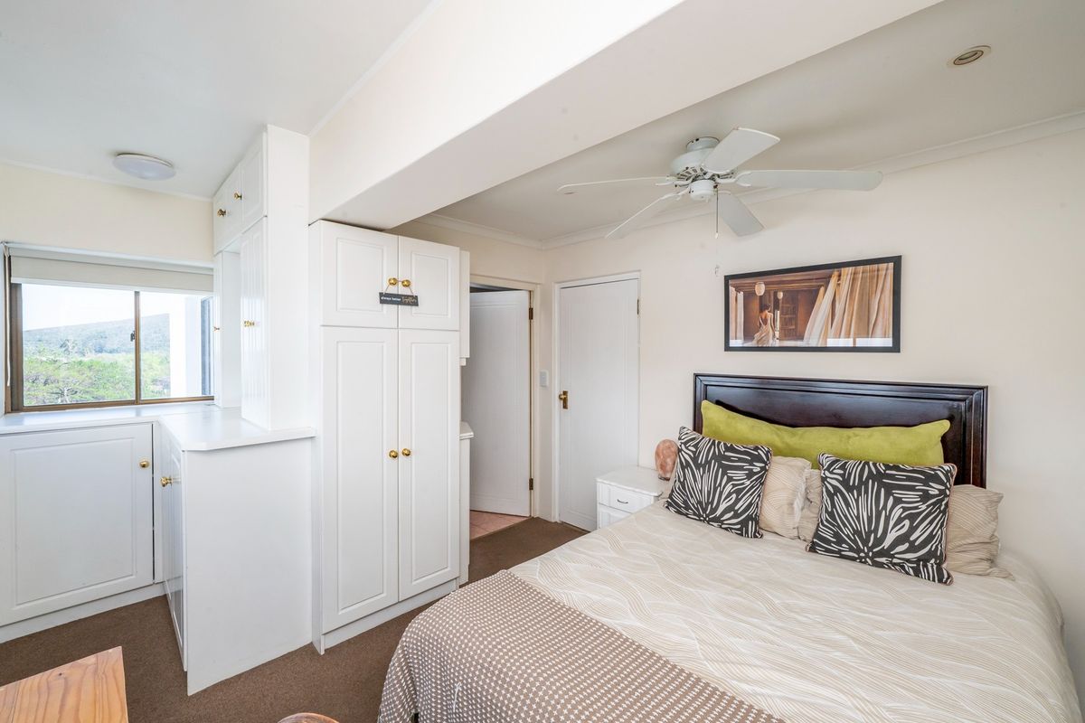 A bedroom featuring built-in white cabinetry, a ceiling fan, and a window with natural light.
