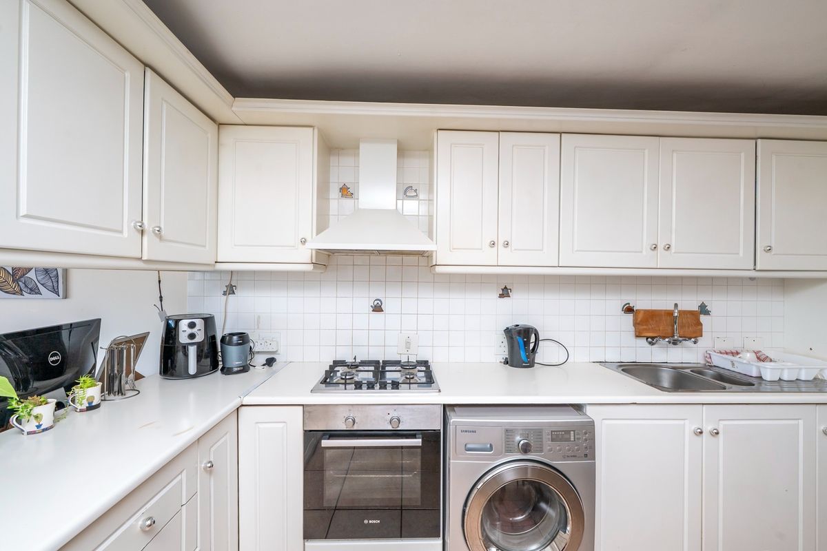 A functional kitchen featuring white cabinetry, a gas hob, built-in oven, extractor fan, and a stainless steel sink with a tiled backsplash.