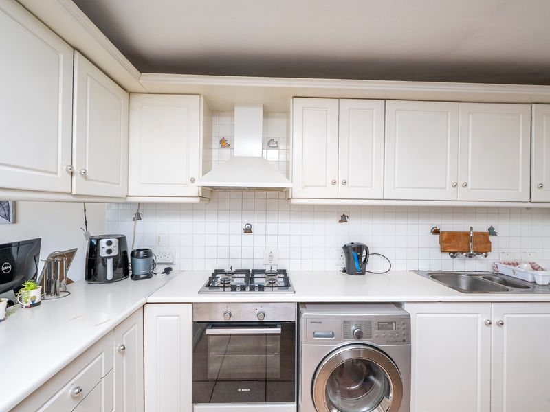 A functional kitchen featuring white cabinetry, a gas hob, built-in oven, extractor fan, and a stainless steel sink with a tiled backsplash.
