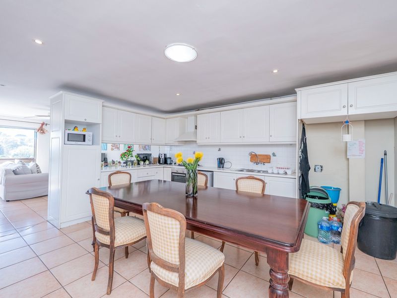Open-plan kitchen and dining area featuring white cabinetry, tiled flooring, and integrated appliances, flowing into a bright living space.