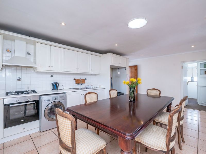 Open-plan kitchen and dining area featuring white cabinetry, built-in appliances, tiled flooring, and a skylight, providing a functional and bright living space.