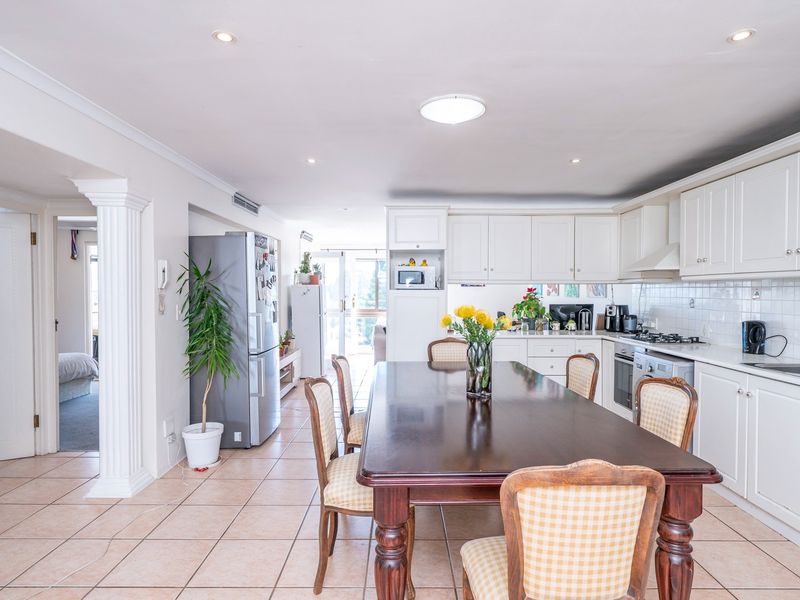 Open-plan kitchen and dining area featuring white cabinetry, tiled flooring, and integrated appliances, creating a functional and connected living space.