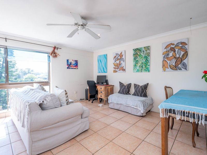 Open-plan living area featuring tiled flooring, a ceiling fan, and large windows providing natural light and exterior views.