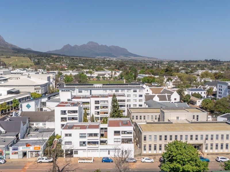 An aerial view of an urban apartment complex and surrounding commercial buildings with mountain views in the background.