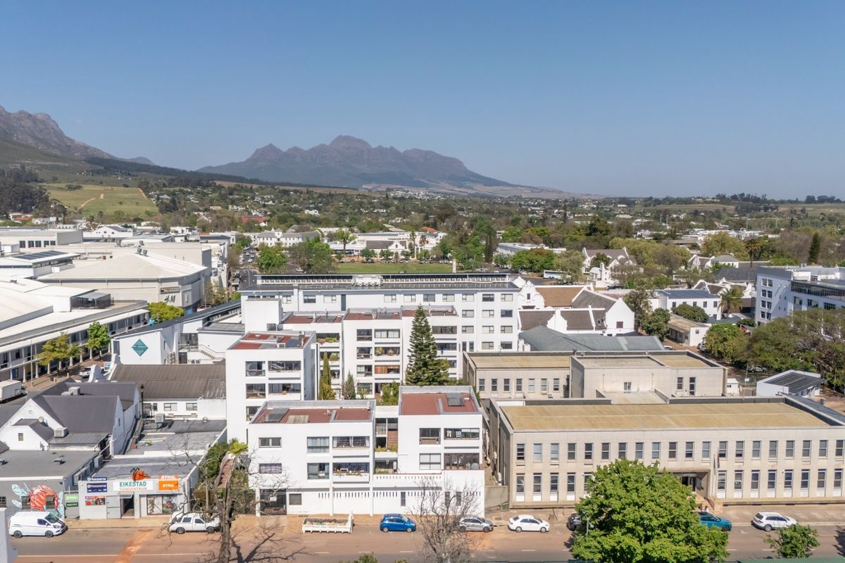 An aerial view of an urban apartment complex and surrounding commercial buildings with mountain views in the background.