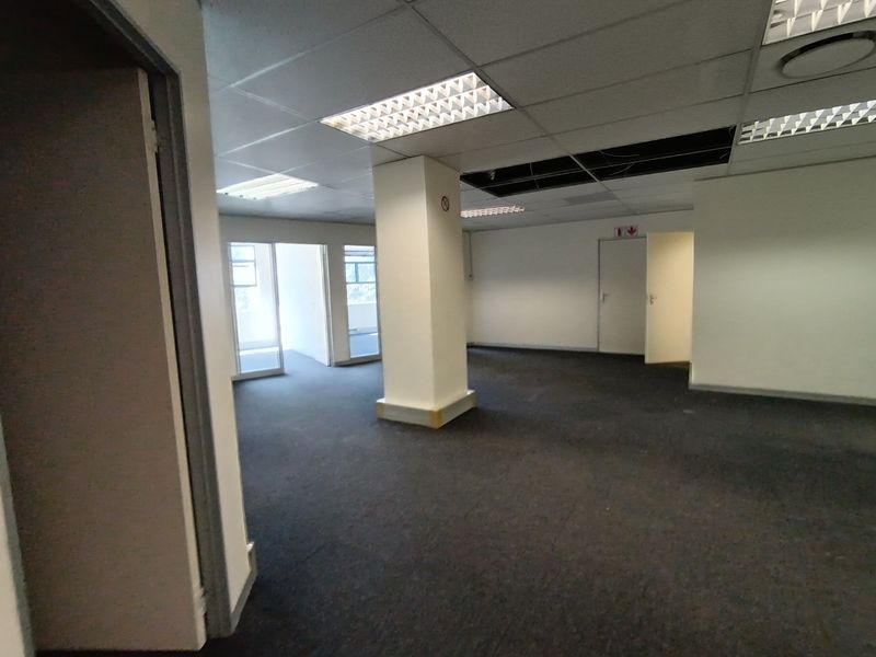 An open-plan office space featuring a suspended ceiling, carpeted flooring, and a central structural column, currently vacant and requiring ceiling repairs.