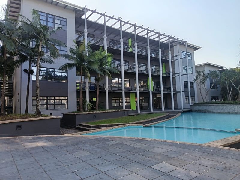 Modern multi-story office building exterior featuring a swimming pool, paved terrace area, and integrated balcony structures with contemporary architectural design.