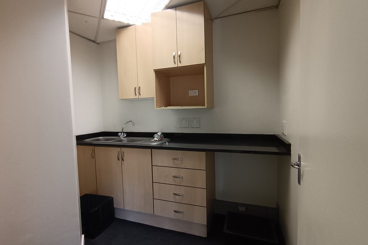 A functional office kitchenette featuring light wood cabinetry, a dark laminate countertop, stainless steel sink, and integrated electrical outlets.