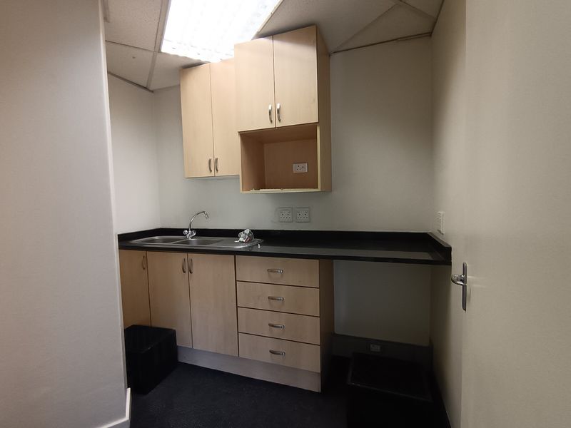 A functional office kitchenette featuring light wood cabinetry, a dark laminate countertop, stainless steel sink, and integrated electrical outlets.