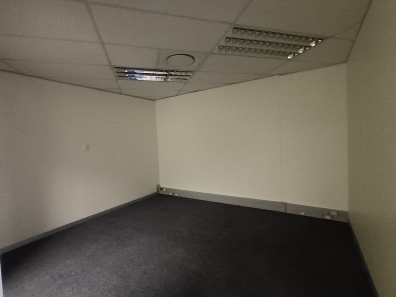 A vacant office space featuring a suspended ceiling with recessed lighting, grey carpeting, and perimeter electrical outlets.