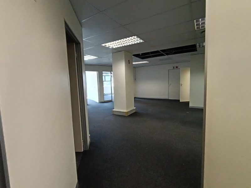 An empty open-plan office space featuring carpeted flooring, a suspended ceiling with recessed lighting, and a central support column, requiring minor ceiling repairs.