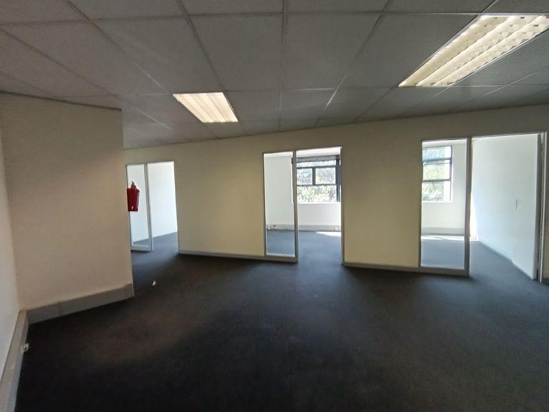 An open-plan office space featuring suspended ceilings, recessed lighting, and glass-partitioned private offices with carpeted flooring.
