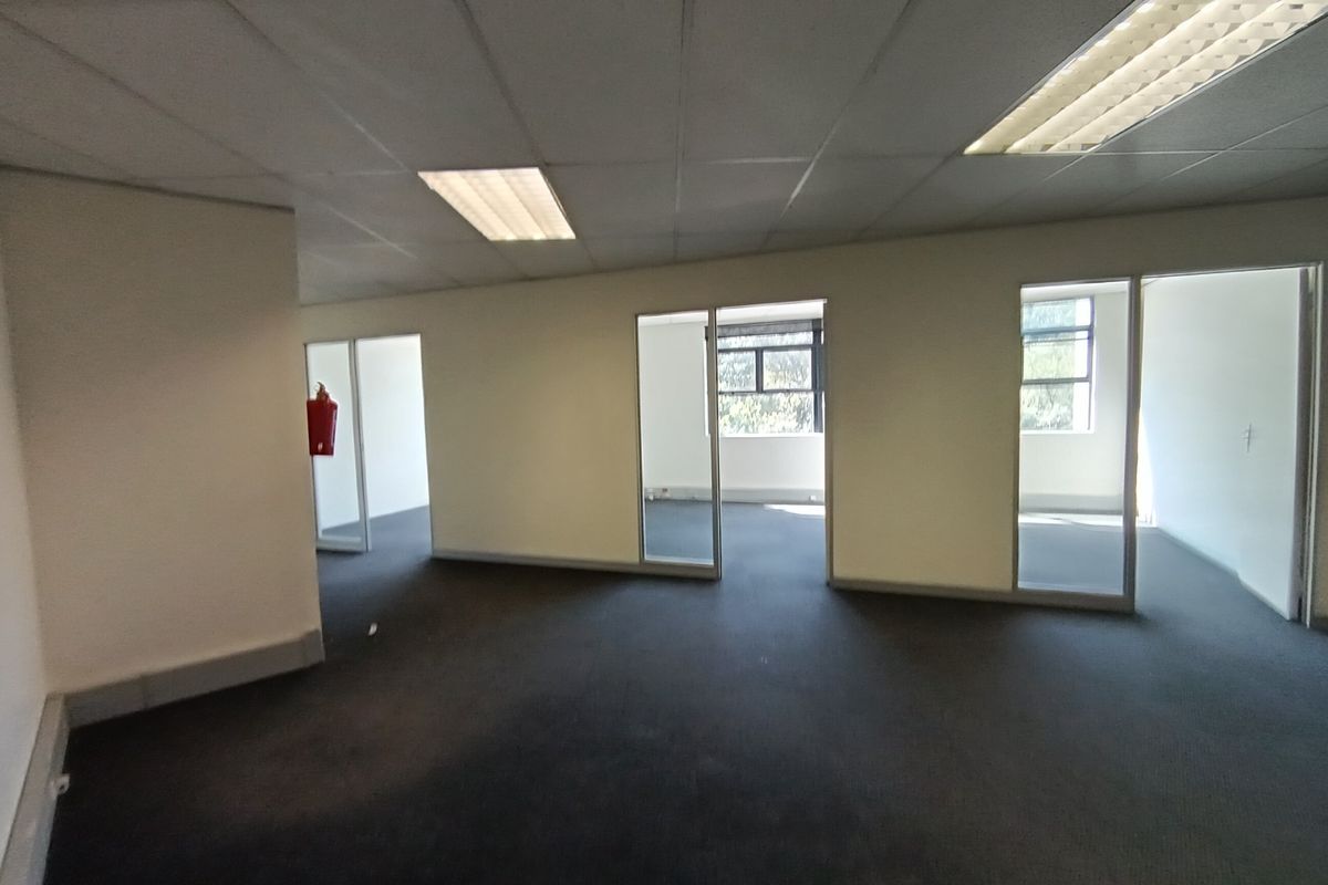 An open-plan office space featuring suspended ceilings, recessed lighting, and glass-partitioned private offices with carpeted flooring.