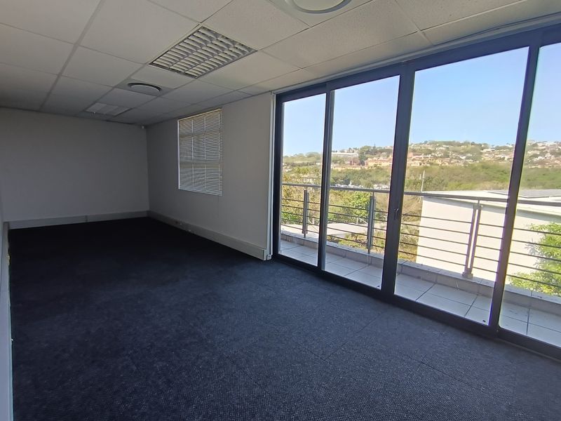 An empty office space featuring carpeted flooring, a suspended ceiling with recessed lighting, and large sliding glass doors leading to a balcony with scenic views.