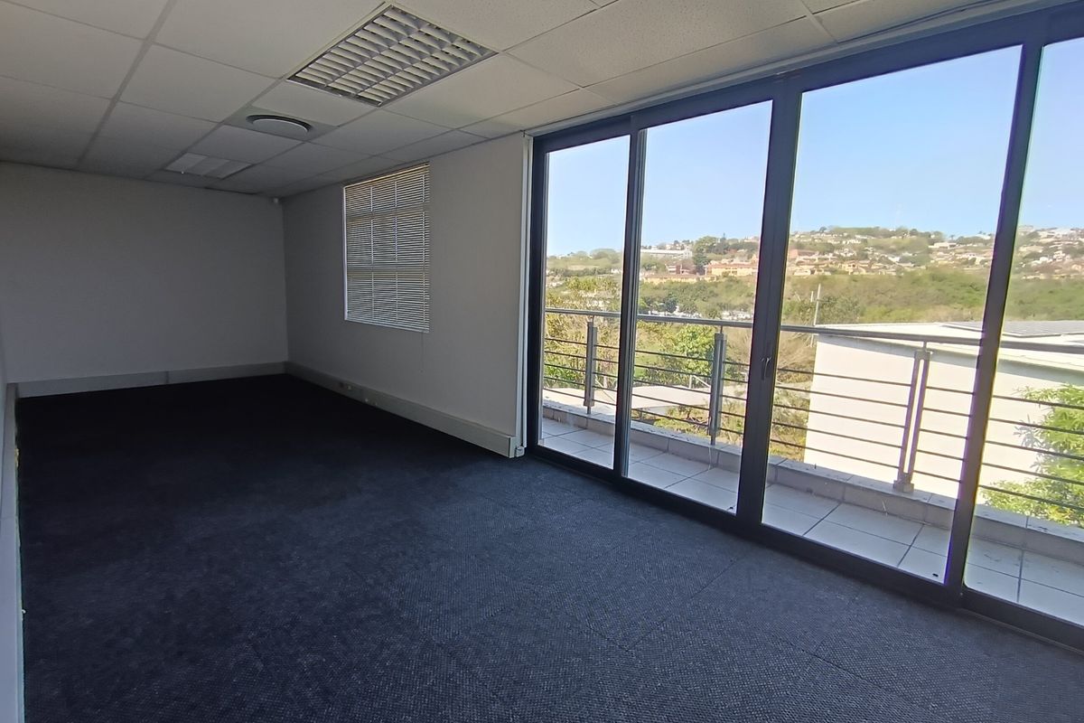 An empty office space featuring carpeted flooring, a suspended ceiling with recessed lighting, and large sliding glass doors leading to a balcony with scenic views.