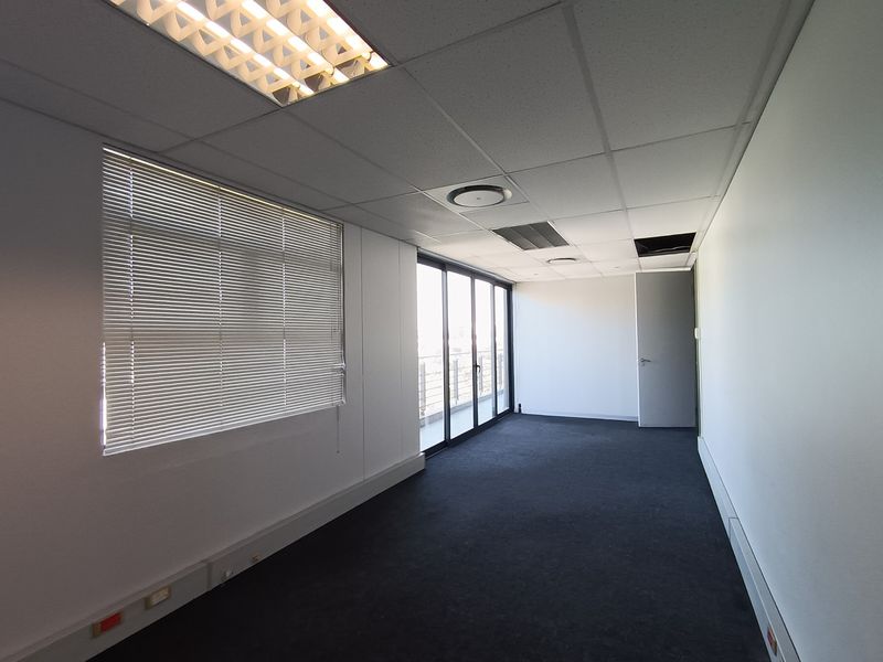 An empty office space featuring a suspended ceiling, carpeted flooring, and large sliding doors leading to a balcony, providing ample natural light.