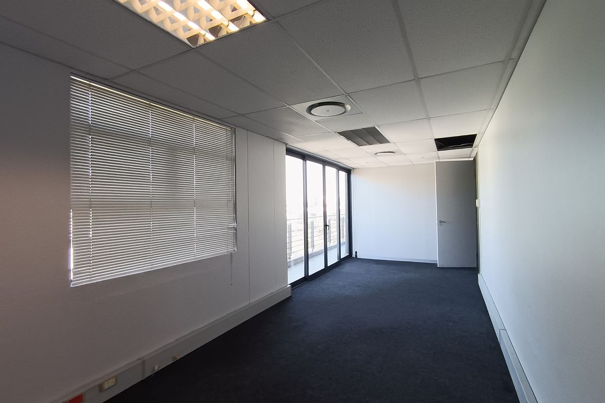 An empty office space featuring a suspended ceiling, carpeted flooring, and large sliding doors leading to a balcony, providing ample natural light.
