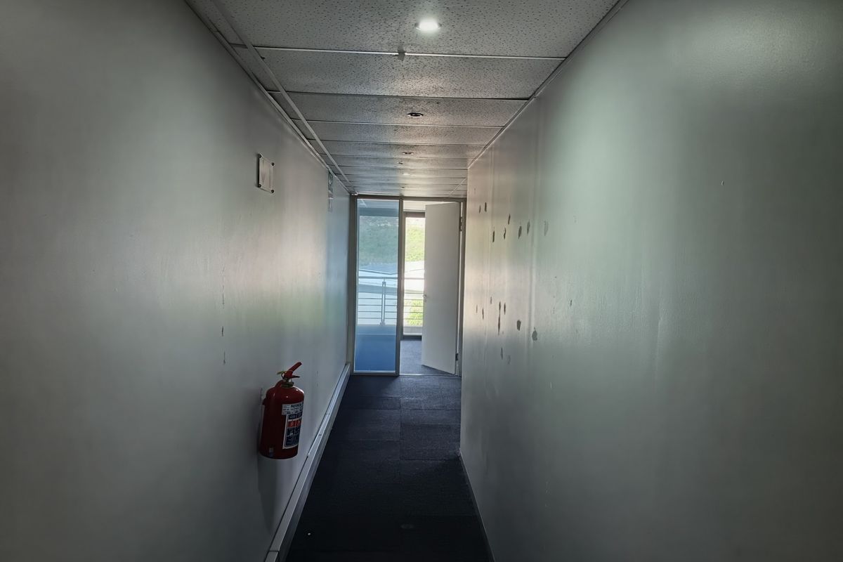 A functional office hallway featuring a suspended ceiling, recessed lighting, and carpeted flooring, leading to an exterior access point.