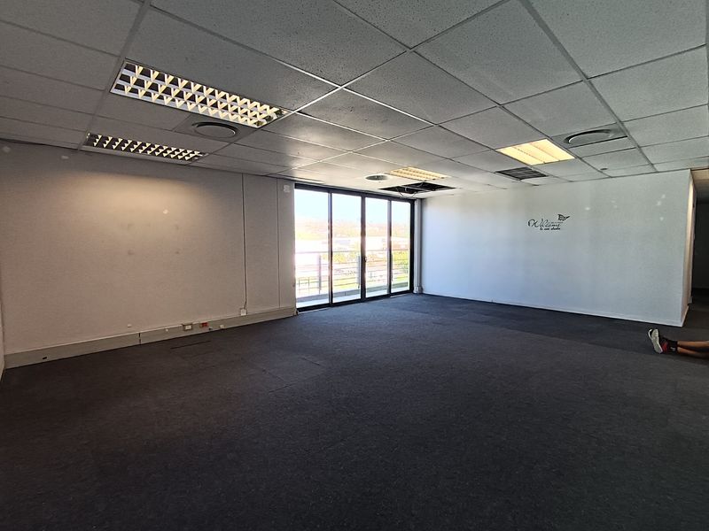 Spacious open-plan office area featuring a suspended ceiling, carpeted flooring, and large sliding glass doors providing natural light.