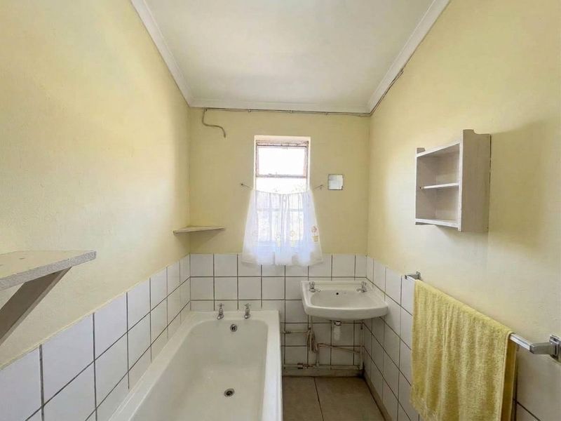 A dated bathroom featuring a standard bathtub, wall-mounted basin, and tiled splashbacks, requiring cosmetic updates to modernize the space.