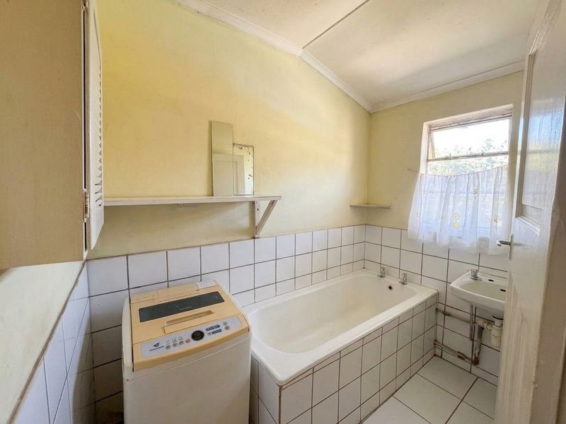 A functional bathroom featuring a bathtub, wall-mounted basin, and tiled finishes, offering potential for modernization and cosmetic updates.