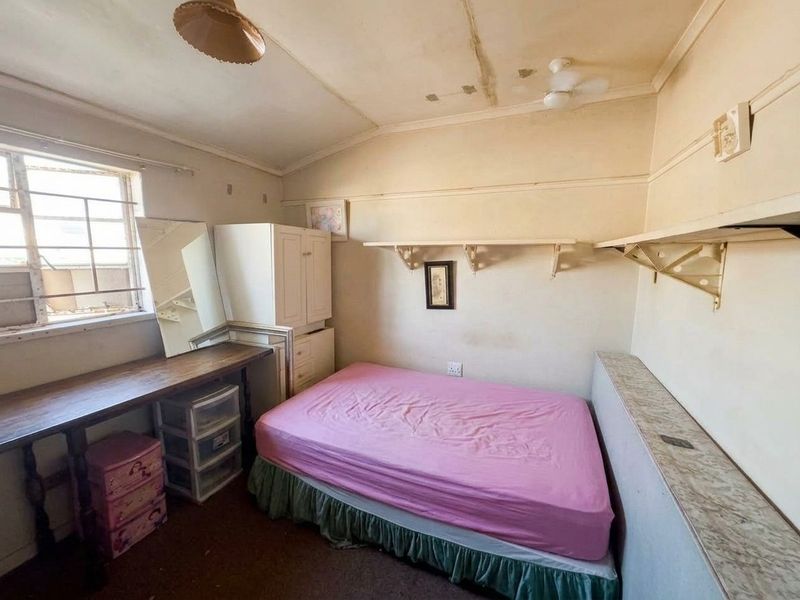 A bedroom featuring built-in shelving, a desk, and a ceiling fan, currently requiring significant cosmetic updates and ceiling repairs.