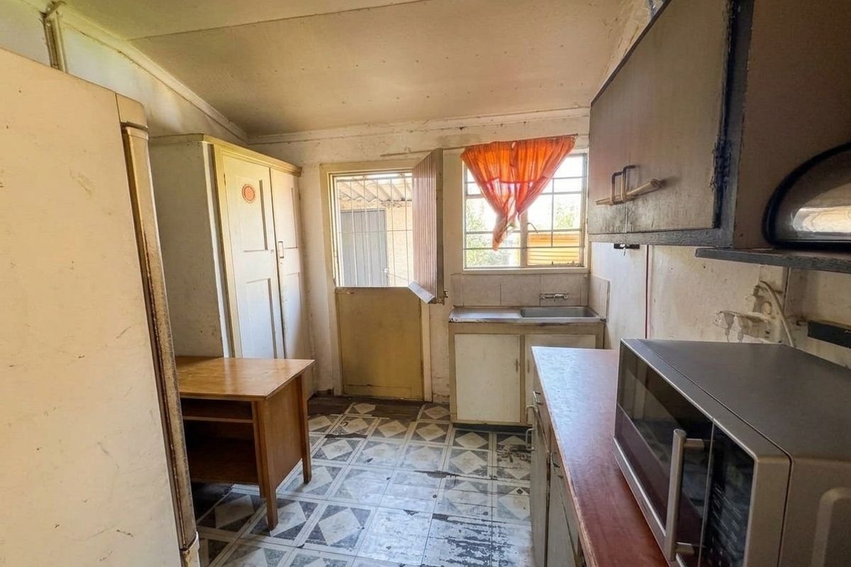 A dated kitchen featuring original cabinetry, tiled flooring, and a rear access door with a security gate, requiring significant renovation and modernization.
