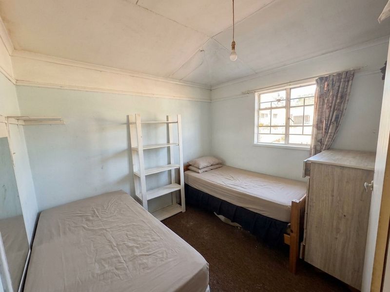 A bedroom featuring security bars on the window, coved ceilings, and worn flooring. The room requires cosmetic updates and repairs to the ceiling and walls.