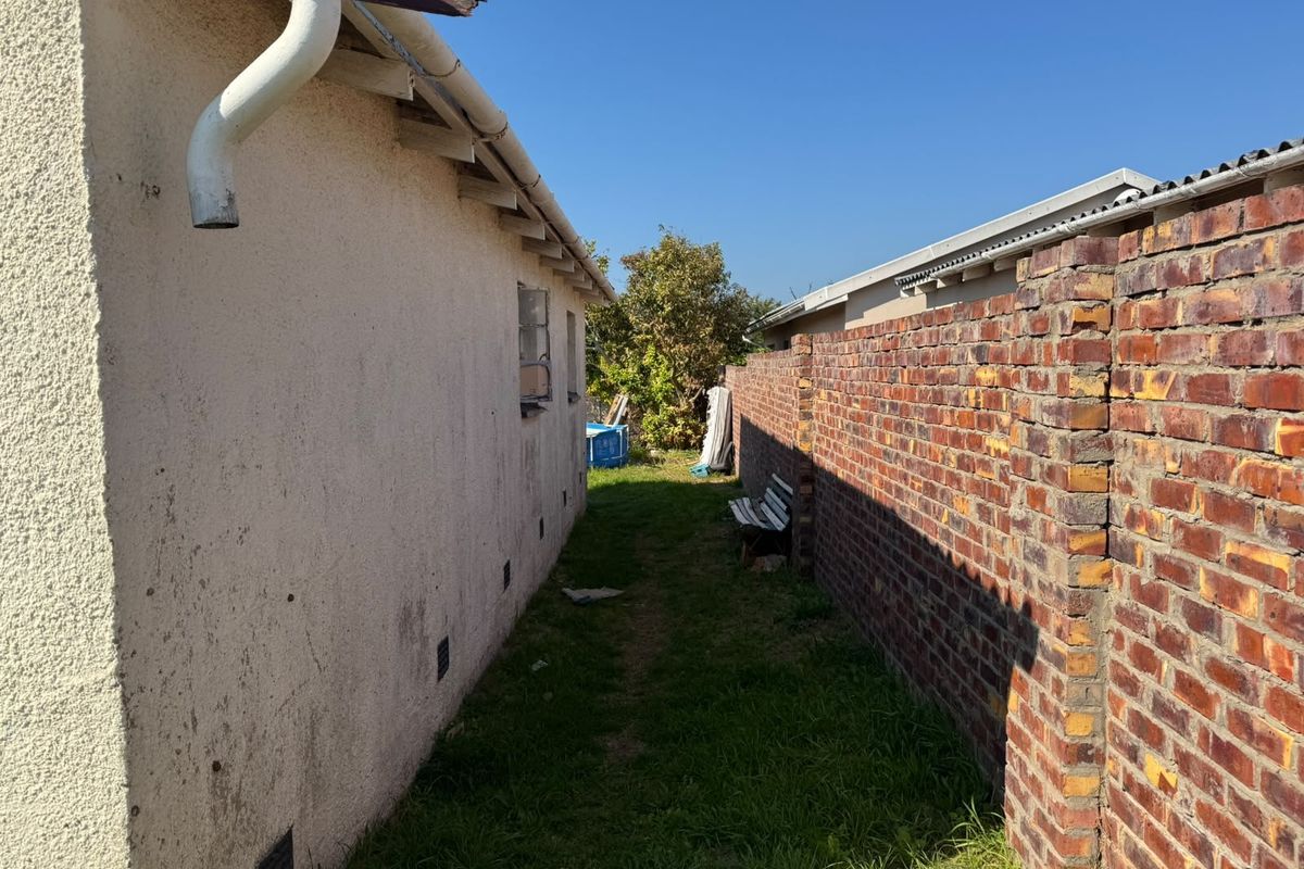 A narrow side passage between the house exterior and a brick boundary wall, featuring a damaged gutter and weathered wall finishes.