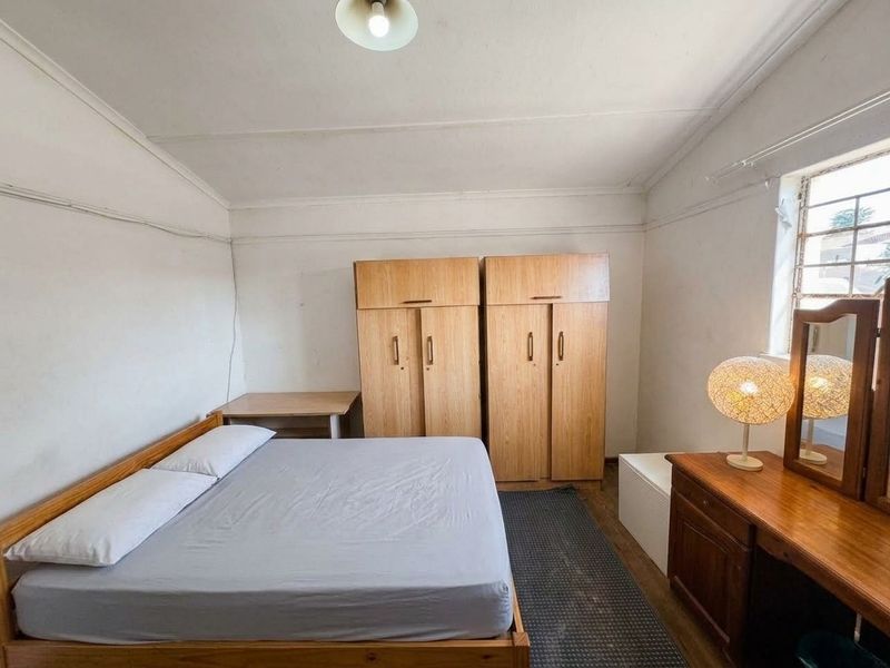 A functional bedroom featuring built-in wooden cupboards and a window with security bars, offering a blank canvas for potential cosmetic updates.