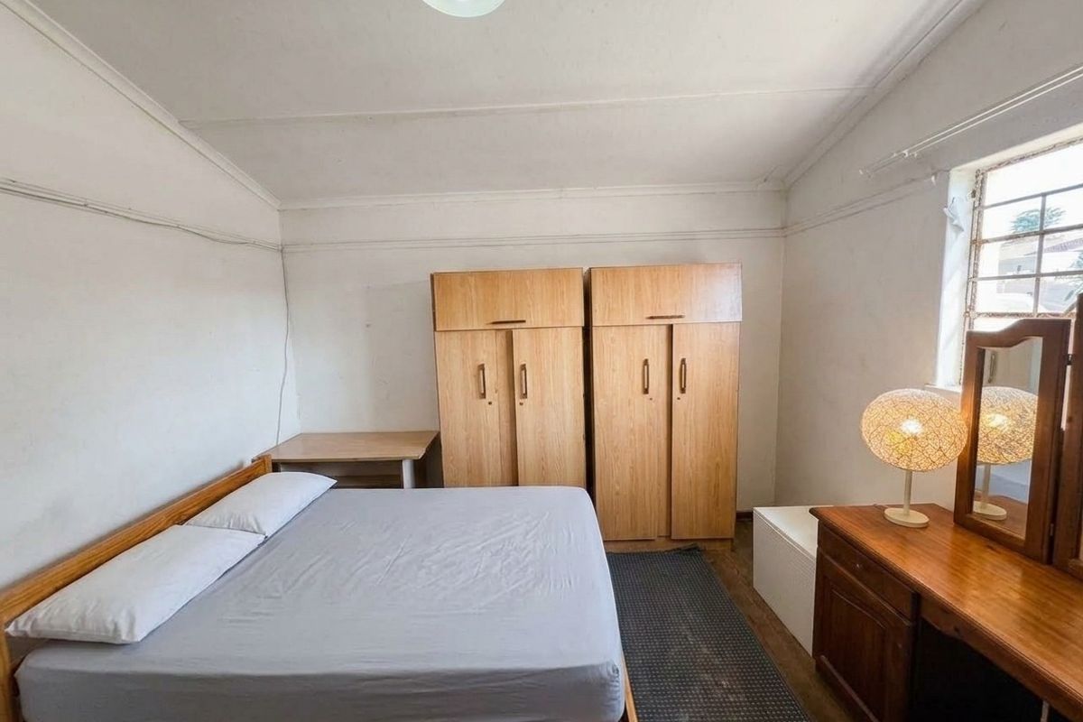 A functional bedroom featuring built-in wooden cupboards and a window with security bars, offering a blank canvas for potential cosmetic updates.