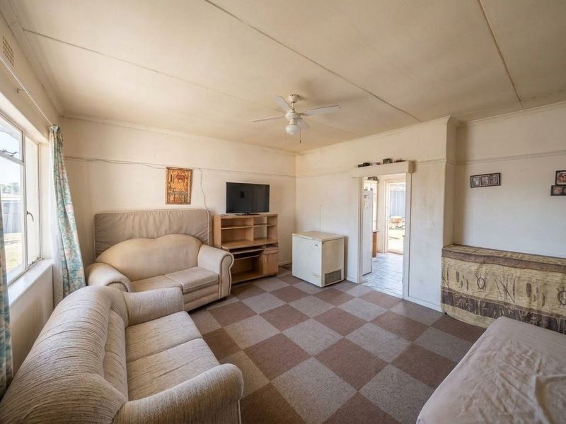 A dated living room featuring a ceiling fan and checkered floor tiles, offering a functional space with potential for modernization and cosmetic updates.