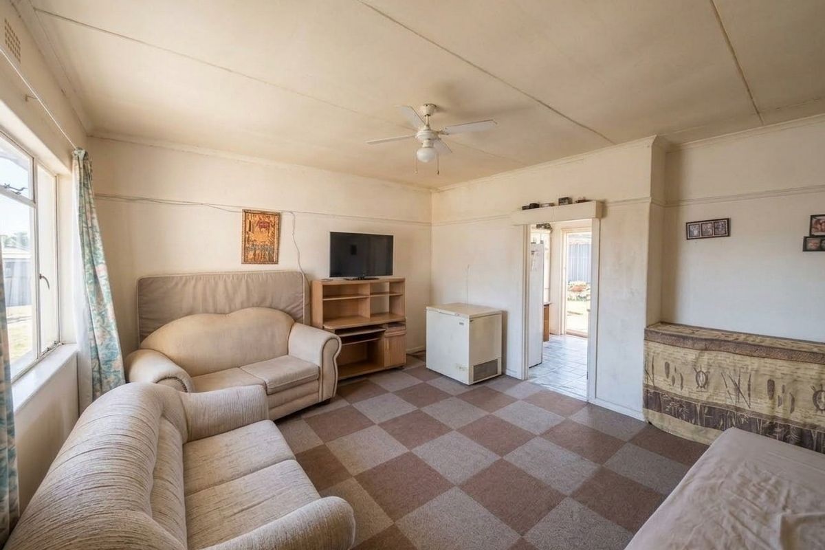 A dated living room featuring a ceiling fan and checkered floor tiles, offering a functional space with potential for modernization and cosmetic updates.