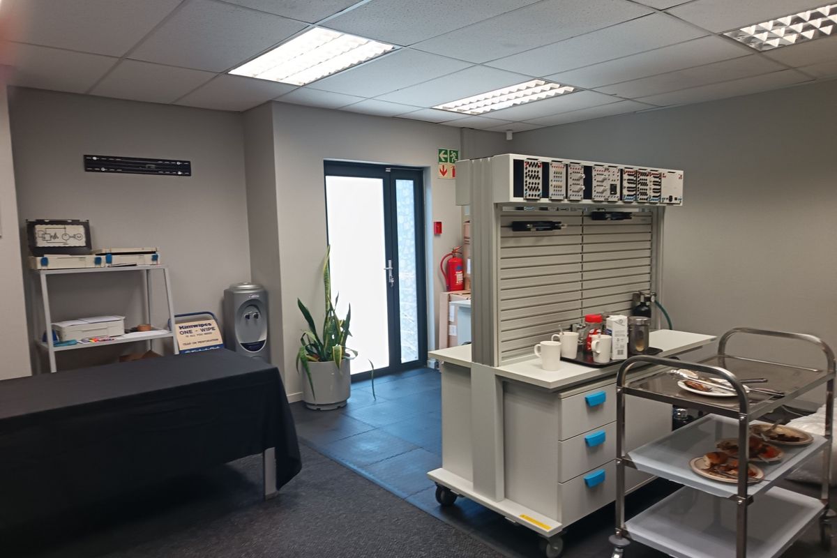 A functional office space featuring a suspended ceiling with recessed lighting, tiled flooring, and a glass panel door providing exterior access.