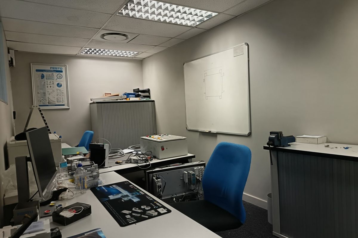 A functional office space featuring a suspended ceiling, recessed lighting, and a wall-mounted whiteboard, suitable for technical or administrative work.