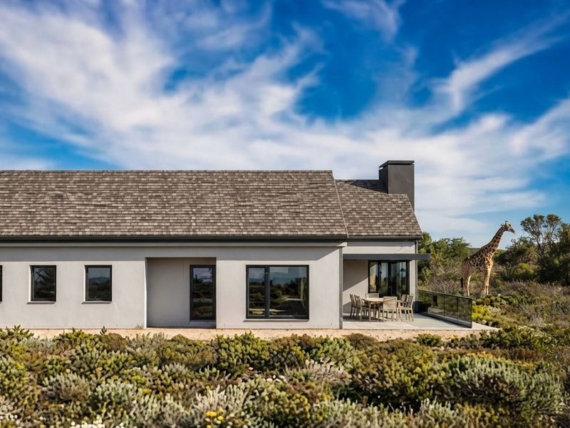 Rear view of a modern single-story home featuring a paved patio, glass balustrade, and a chimney, set against a natural landscape.