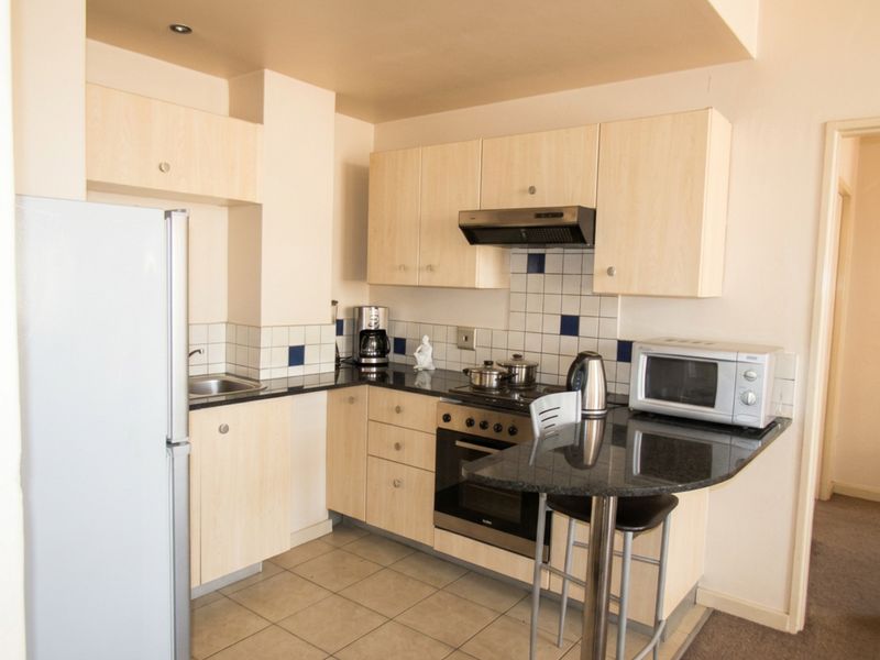 Compact kitchen featuring light wood cabinetry, granite countertops, a built-in oven with extractor fan, and tiled flooring.