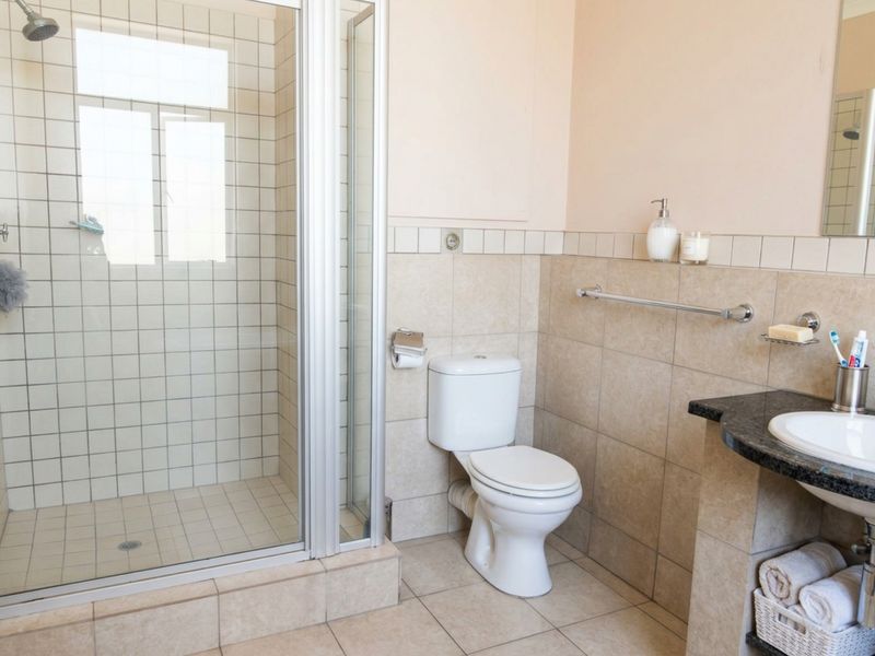 A functional bathroom featuring a glass-enclosed shower, a standard toilet, and a vanity basin with a granite countertop and tiled finishes.