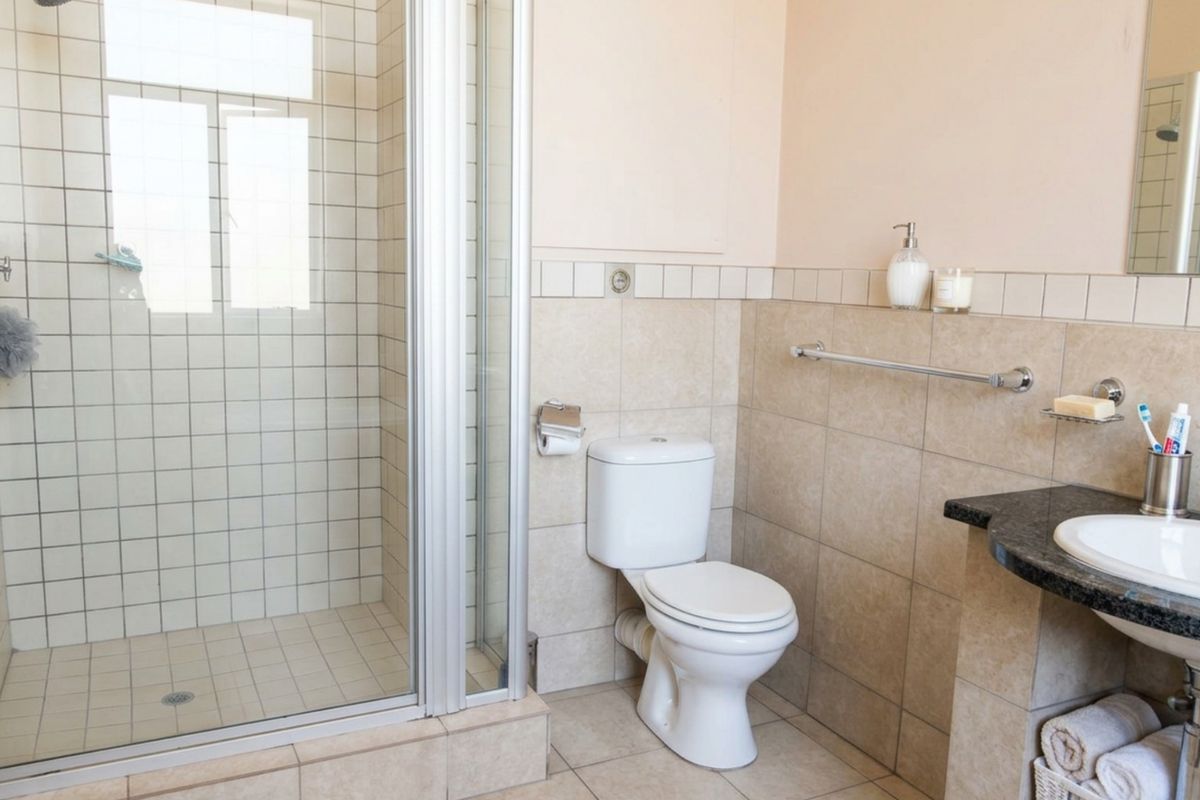 A functional bathroom featuring a glass-enclosed shower, a standard toilet, and a vanity basin with a granite countertop and tiled finishes.