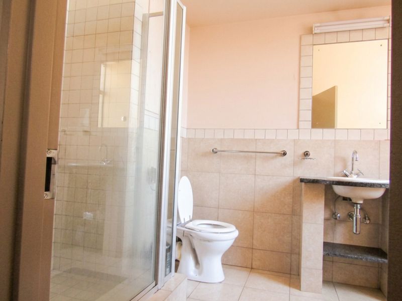 A functional bathroom featuring a shower enclosure, toilet, and a vanity basin with a wall-mounted mirror and tiled finishes.