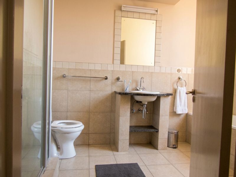 A functional bathroom featuring a shower enclosure, a vanity basin with a granite countertop, and neutral wall and floor tiling.