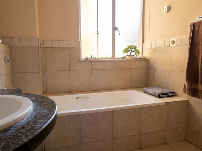 A functional bathroom featuring a built-in bathtub with tiled surround, a vanity countertop with an integrated sink, and natural light from a window.