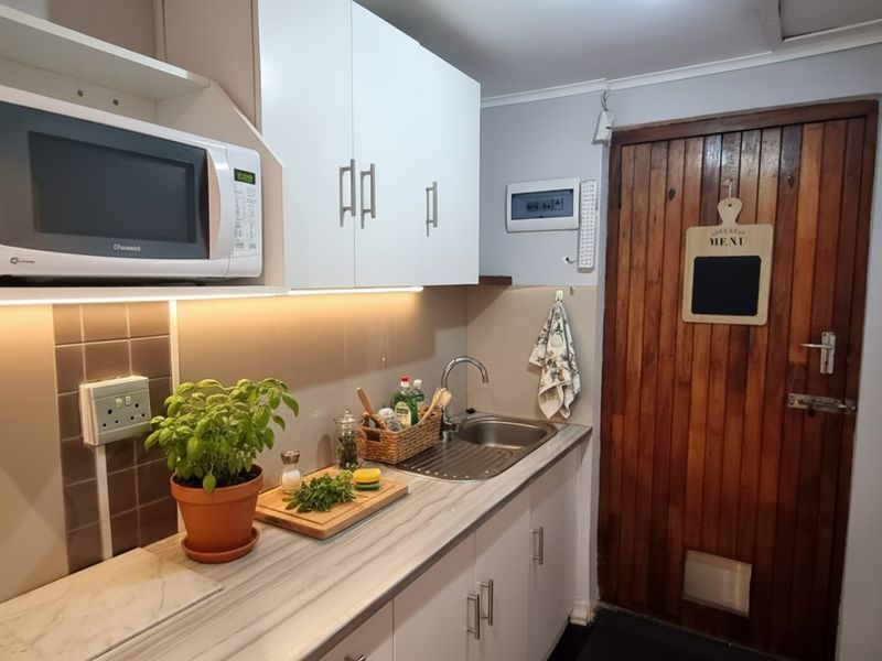 A compact, functional kitchen featuring white cabinetry, laminate countertops, a stainless steel sink, and a built-in microwave with under-cabinet lighting.