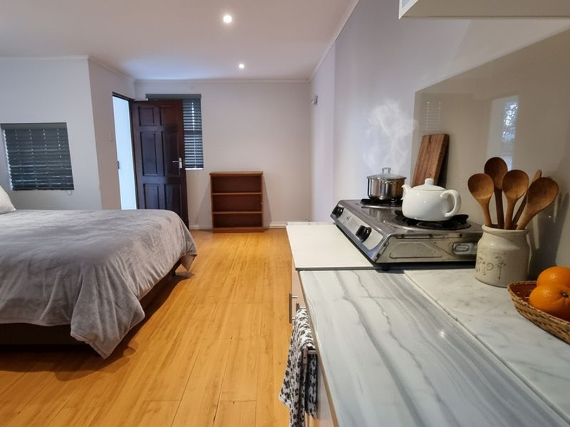 An open-plan studio cottage layout featuring timber flooring, recessed lighting, and a compact kitchenette area with stone-look countertops.