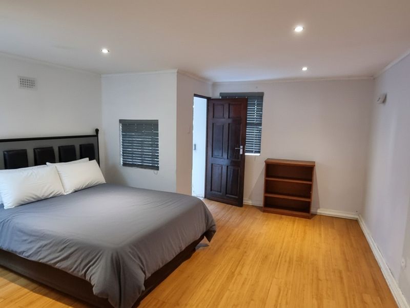 A spacious bedroom featuring laminate flooring, recessed downlighting, and venetian blinds, offering a clean and neutral living space.