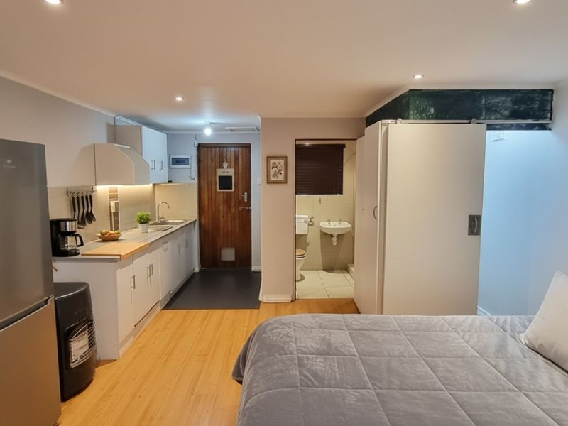 An open-plan studio layout featuring a compact kitchen with modern cabinetry, laminate flooring, and an integrated bathroom access point.