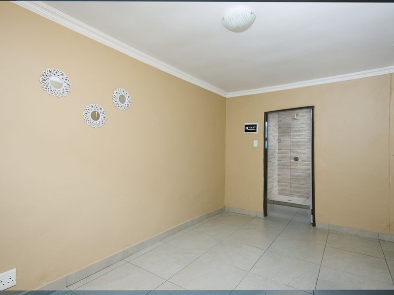 An empty bedroom featuring neutral wall paint, tiled flooring, and direct access to an en-suite shower room.