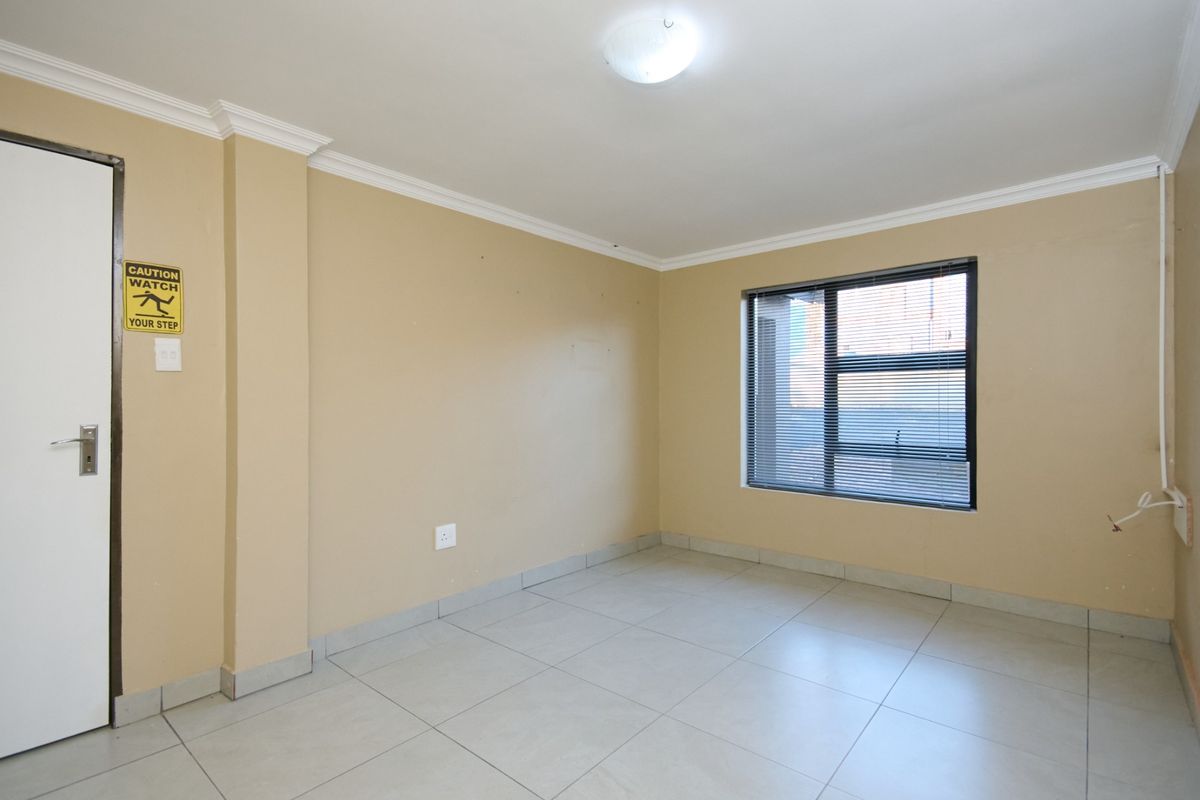 An empty bedroom featuring neutral wall paint, tiled flooring, and an aluminium window with fitted blinds.